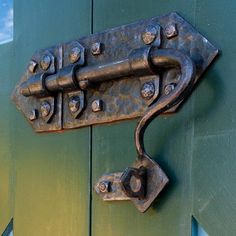 a close up of a metal latch on a green door with blue sky in the background