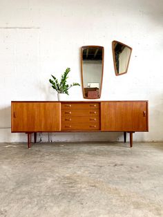 a wooden dresser sitting next to a mirror on top of a white wall with a plant in front of it