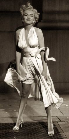 an old photo of a woman in a dress and heels standing on the side walk