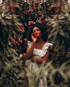 a woman in a white dress is holding a red rose up to her face and looking at the camera