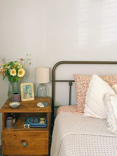 a bed room with a neatly made bed next to a night stand and flowers on the nightstand