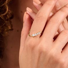 a woman's hand with a gold ring and three stones on it, in front of her face