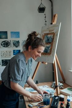 a woman is smiling while painting on an easel