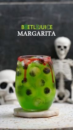 a green drink in a glass with kiwis on the rim and skulls behind it