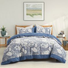 a bed with blue and white comforters in a room next to a painting on the wall