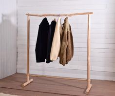 three coats hanging on a clothes rack in front of a white wall and wooden floor