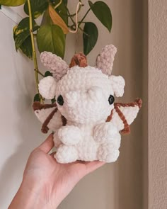 a hand holding a small crocheted stuffed animal in front of a potted plant