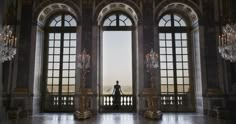 a person standing in front of two large windows with chandeliers hanging from them