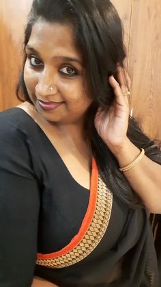 a woman with long black hair is posing for the camera while wearing an orange and black sari