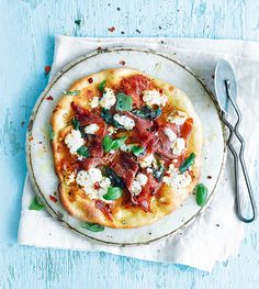 a small pizza with meat and cheese on a plate next to a knife and fork