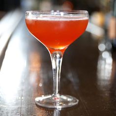 a close up of a drink in a wine glass on a wooden table with blurry background