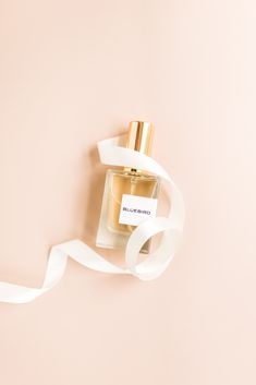 a bottle of perfume sitting on top of a pink wall next to a white ribbon