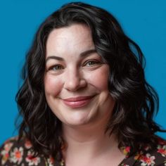 a woman with black hair smiling and wearing a floral shirt, against a blue background