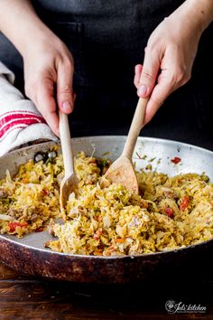 someone is stirring up some food in a skillet with a wooden spoon on the side