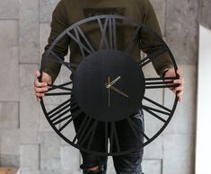 a man holding a large black clock with roman numerals