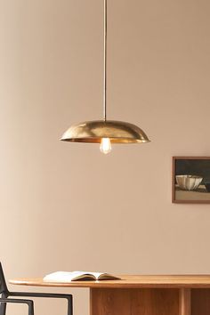 an open book on a table next to a chair and lamp hanging from the ceiling