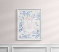 a white frame hanging on the wall above a fireplace with a pink bow and blue flowers