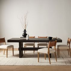 a dining room table with chairs and a vase on the top, in front of a white wall