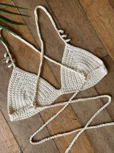 two white crocheted bikinisuits laying on top of a wooden floor next to a plant