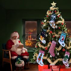 a christmas tree with stockings hanging from it's sides and santa sitting in a chair