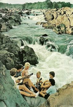 four people are sitting on rocks near a river and playing the ukulele guitar