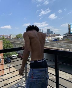 a shirtless man standing on top of a balcony next to a railing looking at the city