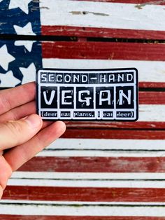 someone holding up a sticker that says vegan in front of an american flag