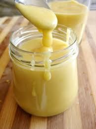 a glass jar filled with yellow liquid sitting on top of a wooden table next to a spoon