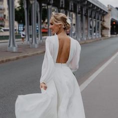 a woman is walking down the street wearing a white dress with open back and long sleeves