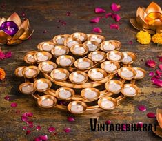 many small candles are placed on the table with petals around them and one candle is surrounded by smaller ones