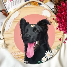 a black dog with its tongue hanging out on a plate next to flowers and books