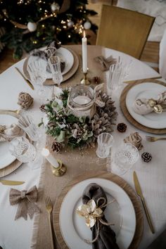 a table set for christmas dinner with pine cones, silverware and candlesticks