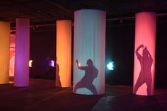 a person standing in front of three tall pillars with colored lights on the walls behind them