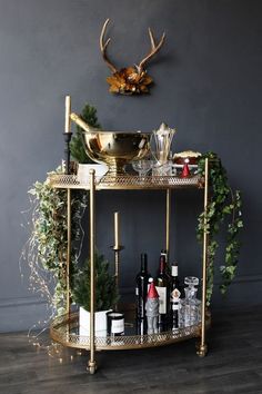 a gold bar cart with bottles and glasses on it in front of a deer head