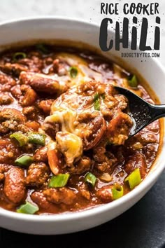 a white bowl filled with chili and meat on top of a black table next to a spoon