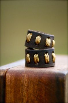 two leather bracelets sitting on top of a piece of wood next to each other