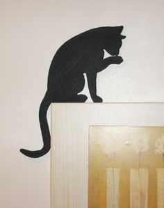 a black cat sitting on top of a wooden frame next to a wall mounted painting