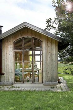 a small wooden building with glass doors on the front and windows in the back, surrounded by green grass