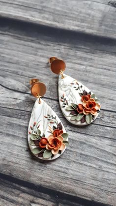 two pairs of white and orange flowered earrings on wooden table with wood planks