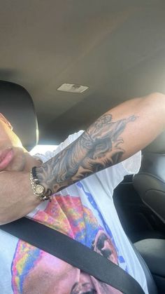 a man with tattoos on his arm sitting in a car