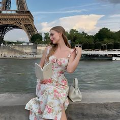 a beautiful young woman sitting on the edge of a wall next to the eiffel tower