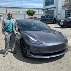 a man in a suit and tie standing next to a silver tesla model 3 car