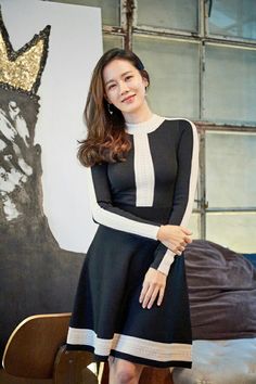 a woman in a black and white dress standing next to a chair with her hands on her hips