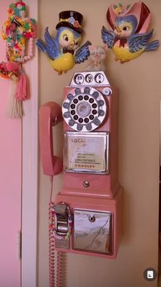 an old fashioned pink phone is hanging on the wall next to two little bird figurines