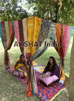 two women sitting on a colorful blanket under a tree