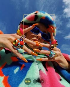 a woman with colorful nails and sunglasses holding up her hand in front of the camera