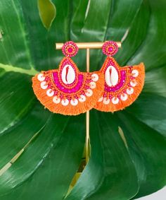 an orange and pink earring hanging from a green plant with leaves in the background