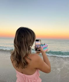 a woman taking a photo on the beach with her cell phone and cake in front of her