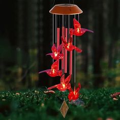 a wind chime with red flowers hanging from it's side in the woods