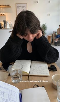 a woman sitting at a table in front of an open book and holding her head